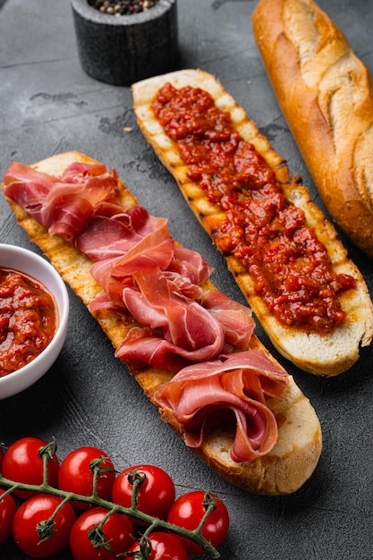 Rebanada de pan tostado con tomates frescos y jamón curado sobre fondo de mesa de piedra gris