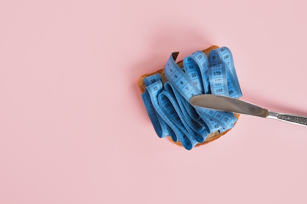 Rebanada de pan de trigo y cinta métrica azul sobre rosa