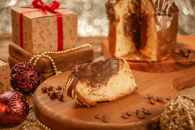 Foto rebanada de panettone de chocolate sobre tabla de cortar de madera con adornos navideños