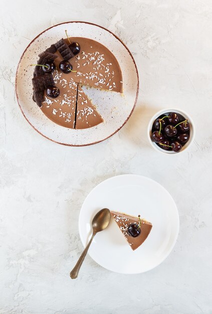 Rebanada de pastel de chocolate crudo con cerezas y plátano sobre un fondo gris