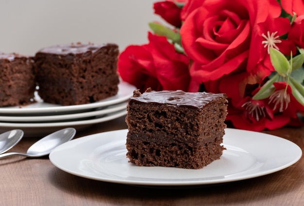 Rebanada de pastel de chocolate cubierto con chocolate servido frío con un ramo de rosas rojas