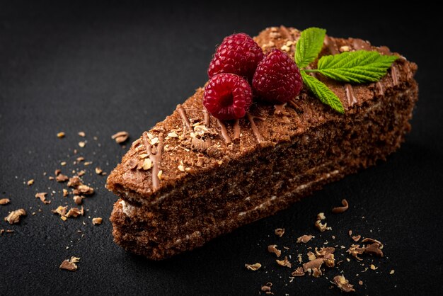 Rebanada de pastel de chocolate con relleno de leche y frambuesa sobre superficie negra.