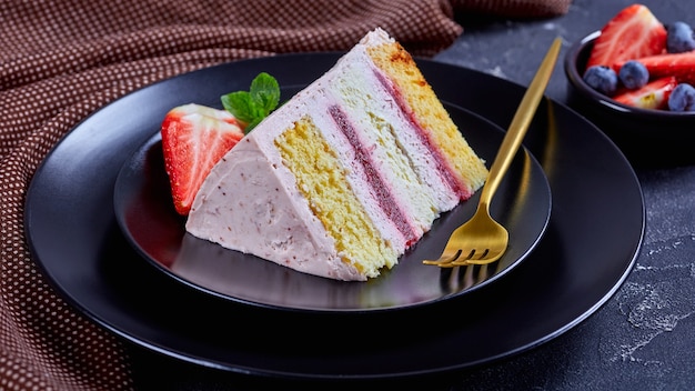 Foto una rebanada de un pastel de fresa rosa servido con bayas frescas en una placa negra con tenedor dorado sobre una mesa de hormigón