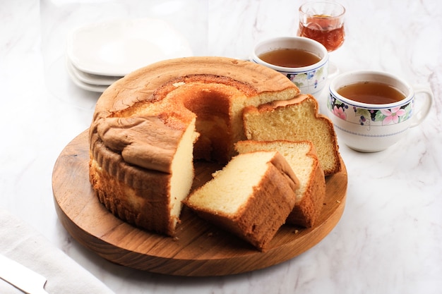 Rebanada de pastel de gasa de vainilla esponjosa o bizcocho en un plato de madera, servido con té y miel. Concepto de fotografía de alimentos brillantes para panadería. Enfoque seleccionado