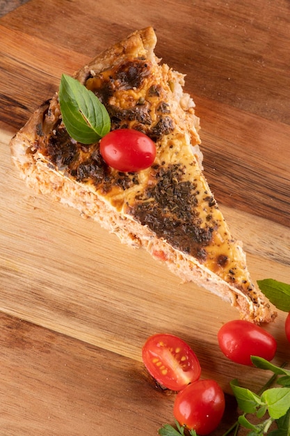 Rebanada de pastel de pollo salado con pasta de orégano y tomates cherry en una tabla redonda de madera en una mesa rústica vista superior