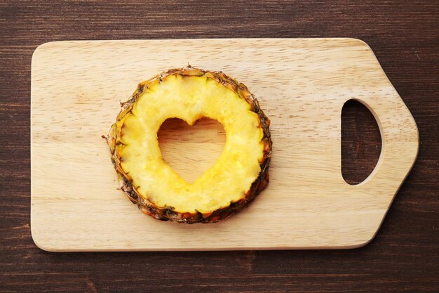 Rebanada de piña con corte en forma de corazón sobre fondo de madera