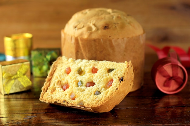 Rebanada de primer del panettone con la tabla de madera de las frutas confitadas. Decoración navideña. frente v