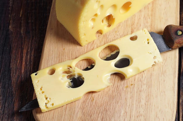 Rebanada de queso y cuchillo sobre fondo de madera