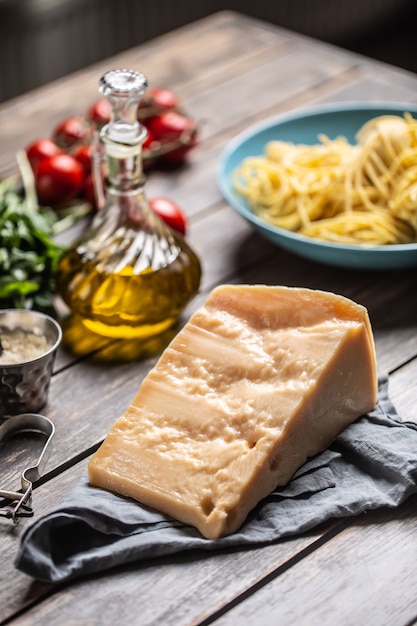 Rebanada de queso parmesano grande sobre una mesa llena de ingredientes para la cocina italiana.