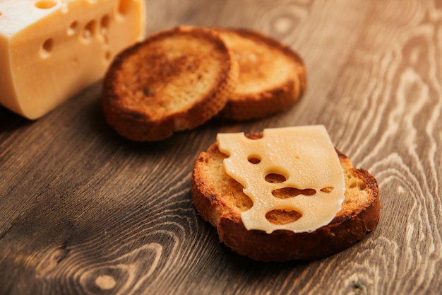 Una rebanada de queso sudoroso y pan frito en una mesa de madera. Queso con grandes agujeros. Sándwich de queso.