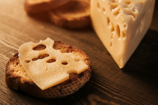 Una rebanada de queso sudoroso y pan frito en una mesa de madera. Queso con grandes agujeros. Sándwich de queso.