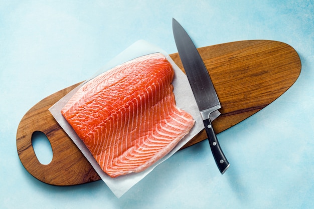 Rebanada de salmón fresco en una tabla de cortar de madera con un cuchillo de chef sobre la mesa. Receta de cocina. Fondo de alimentos. productos de pescado fresco