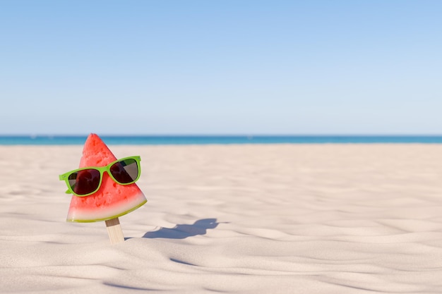 Una rebanada de sandía con gafas de sol en la playa de arena