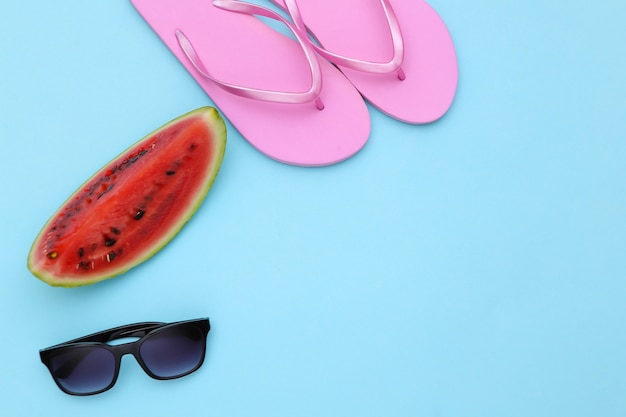 Rebanada de sandía madura, gafas de sol y chanclas sobre fondo azul. Diversión de verano, descanso en la playa. Vista superior. Endecha plana. Copia espacio