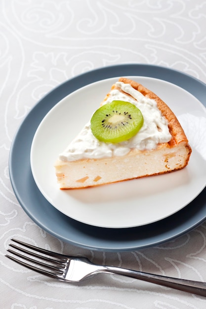 Rebanada de tarta casera de requesón con kiwi y crema en una placa