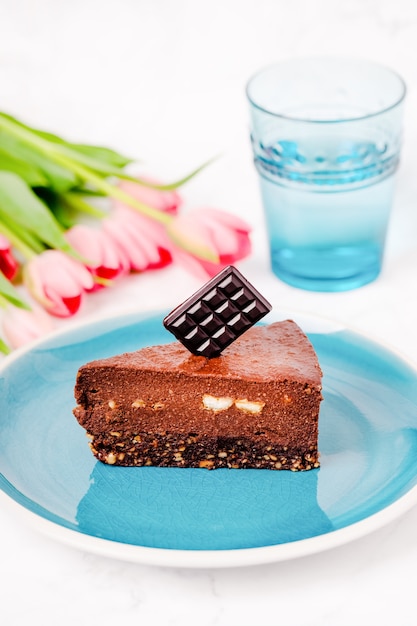 Una rebanada de tarta cruda de brownie de chocolate saludable con avellanas, un vaso de agua y tulipanes rosas