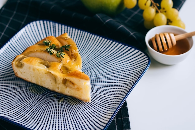 Una rebanada de tarta de manzana fresca con uvas y miel en un plato azul