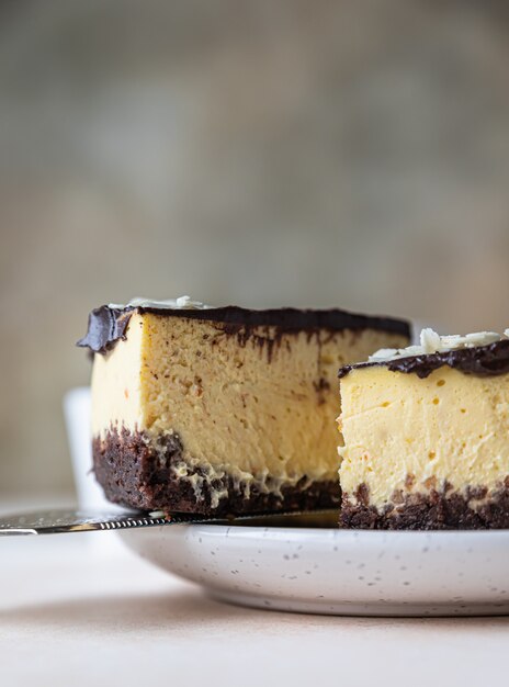 Rebanada de tarta de queso cremoso sin hornear con glaseado de chocolate y almendras, fondo de hormigón claro.