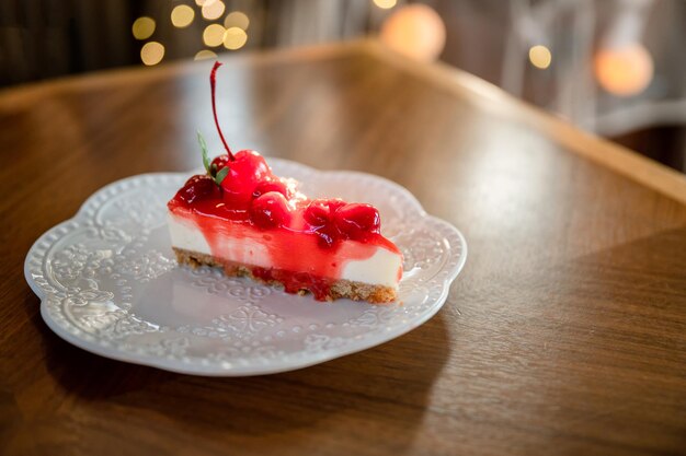 Rebanada de tarta de queso de fresa con capa de galleta cereza y mermelada en un plato blanco en el restaurante