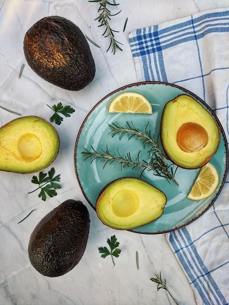 Rebanadas de aguacate fresco con hierbas y limones se encuentran sobre la mesa en un plato azul. Endecha plana. Vista superior.