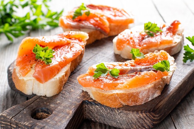Rebanadas de baguette fresco con mantequilla y salmón servido sobre tabla de madera sobre mesa de madera