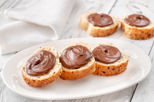 Rebanadas de baguette con pasta de chocolate en la placa blanca.