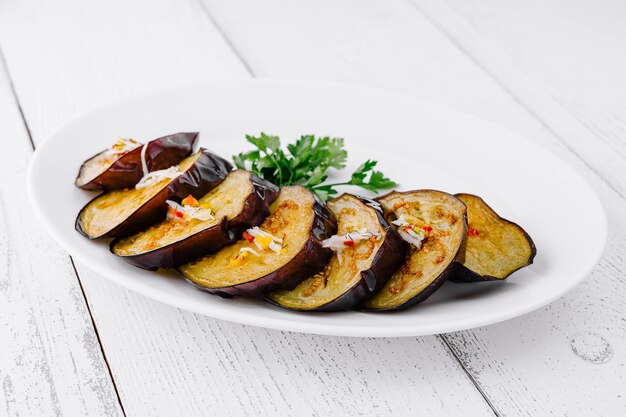 Rebanadas de berenjena a la parrilla con ajo y hierbas en un plato blanco