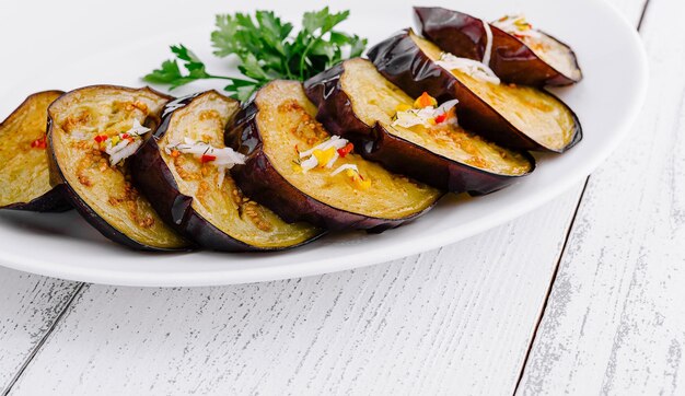 Rebanadas de berenjena a la parrilla con ajo y hierbas en un plato blanco