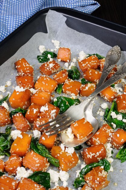 Rebanadas de calabaza al horno con espinacas y semillas de sésamo en una bandeja para hornear