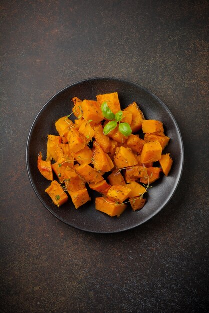 Rebanadas de calabaza frita con hierbas y pimienta, aceite de oliva en una placa de cerámica negra sobre hormigón oscuro o piedra