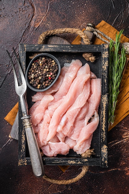 Rebanadas de carne de pollo cruda sin cocer en una bandeja de madera con hierbas Fondo oscuro Vista superior