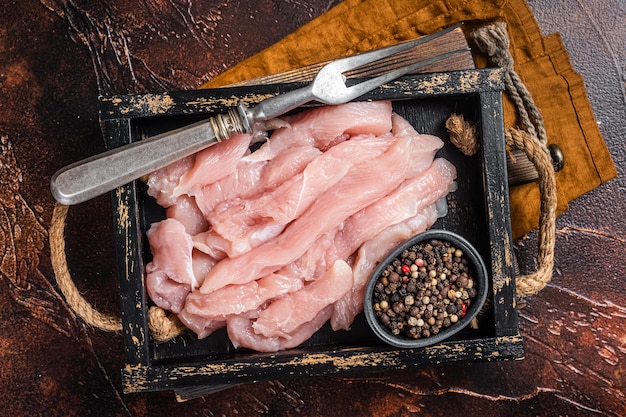 Rebanadas de carne de pollo cruda sin cocer en una bandeja de madera con hierbas Fondo oscuro Vista superior