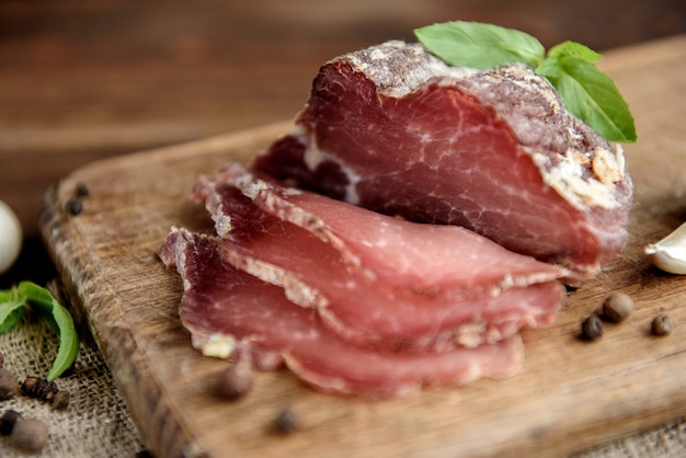 Rebanadas de carne seca de cerdo sobre fondo rústico de madera oscura. Jamón de salami de prosciutto de cerdo seco con hierbas.