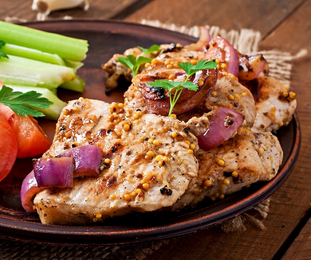 Rebanadas de cerdo a la parrilla con verduras en placa de cerámica marrón.