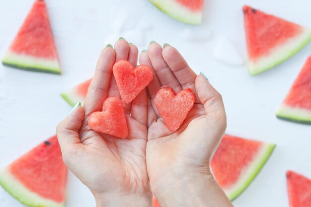 Rebanadas de corazones de sandía en manos de mujer. Sandía en rodajas sobre fondo blanco. Vista plana endecha, superior. Concepto de amor y cuidado.