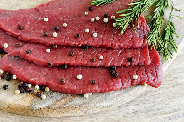 Rebanadas crudas de carne magra con pimienta y romero en la tabla de cortar