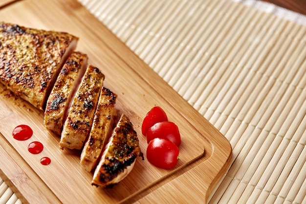 Rebanadas de filete de pollo frito sobre una tabla para cortar con rodajas de tomate sobre una estera de bambú