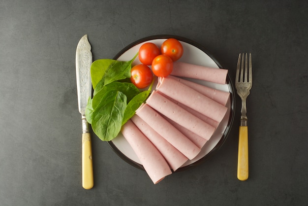 Rebanadas finas de jamón enrolladas en un plato con verduras frescas