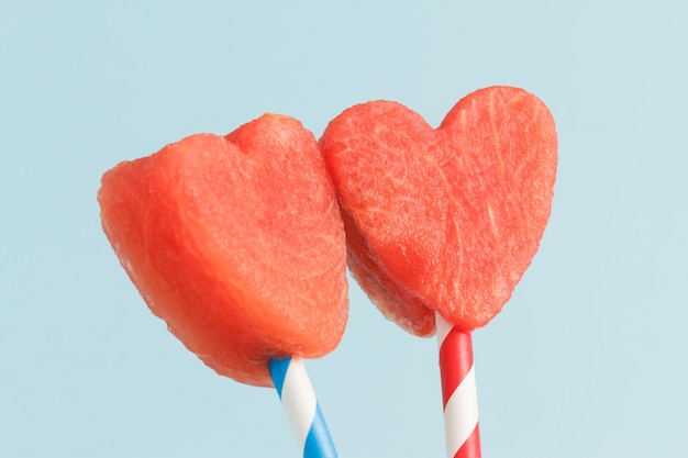 Rebanadas en forma de corazón de la sandía en las pajas en fondo azul