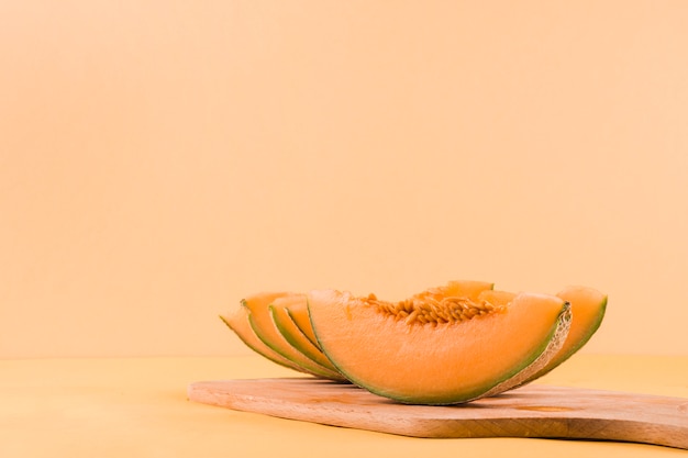 Rebanadas de frutas del cantalupo en la tajadera contra el contexto coloreado