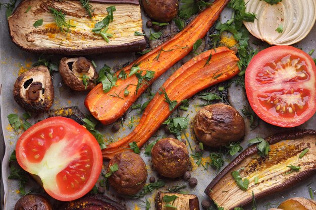 Rebanadas horneadas de berenjena remolacha zanahorias cebollas patatas champiñones enteros especias hierbas y mitades de tomate en papel pergamino comida vegetariana primer plano