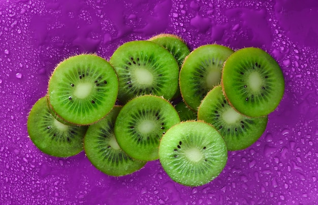 Las rebanadas de kiwi en agua caen en un fondo púrpura. Concepto de fruta.