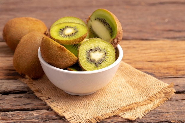 Rebanadas de kiwis frescos en un cuenco blanco en el saco marrón colocado en la vieja mesa de madera