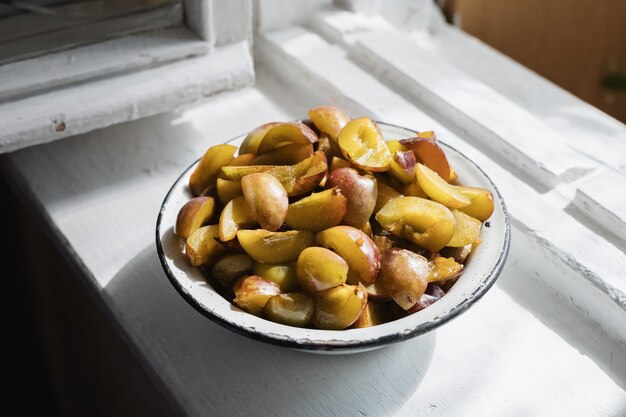 Rebanadas maduras frescas de ciruelas deshuesadas se encuentran en un recipiente de metal sobre un alféizar blanco