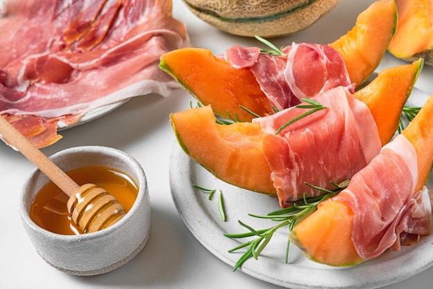 Rebanadas de melón con jamón prosciutto, romero y miel en un plato sobre fondo blanco Aperitivo italiano