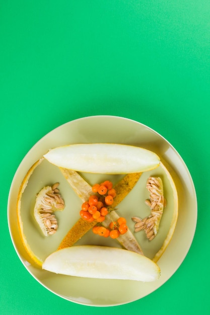 Rebanadas de melón semillas y pieles de melón en un plato verde Melón y bayas de serbal sobre fondo verde Comida vegetariana saludable Vista superior Copiar espacio