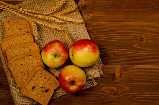 Rebanadas de pan de centeno, tres manzanas, espigas de trigo en saqueo, mesa de madera, vista superior