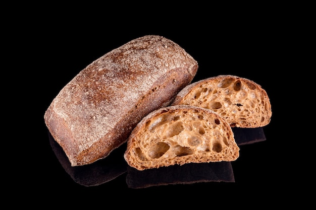 Rebanadas de pan ciabatta italiano oscuro. Pan casero recién horneado aislado en negro. Alimentación saludable y panadería tradicional, concepto de pan para hornear.