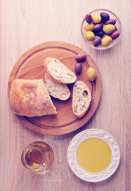 Rebanadas de pan ciabatta sobre tabla redonda, aceitunas y aceite de oliva virgen extra