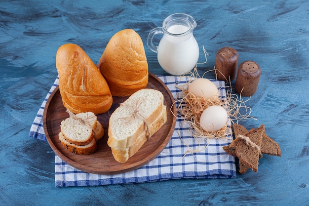 Rebanadas de pan, jarra de leche y huevo sobre un paño de cocina, sobre la superficie azul.